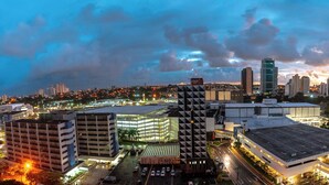 A cityscape at dusk with modern buildings, a parking structure, and a river.