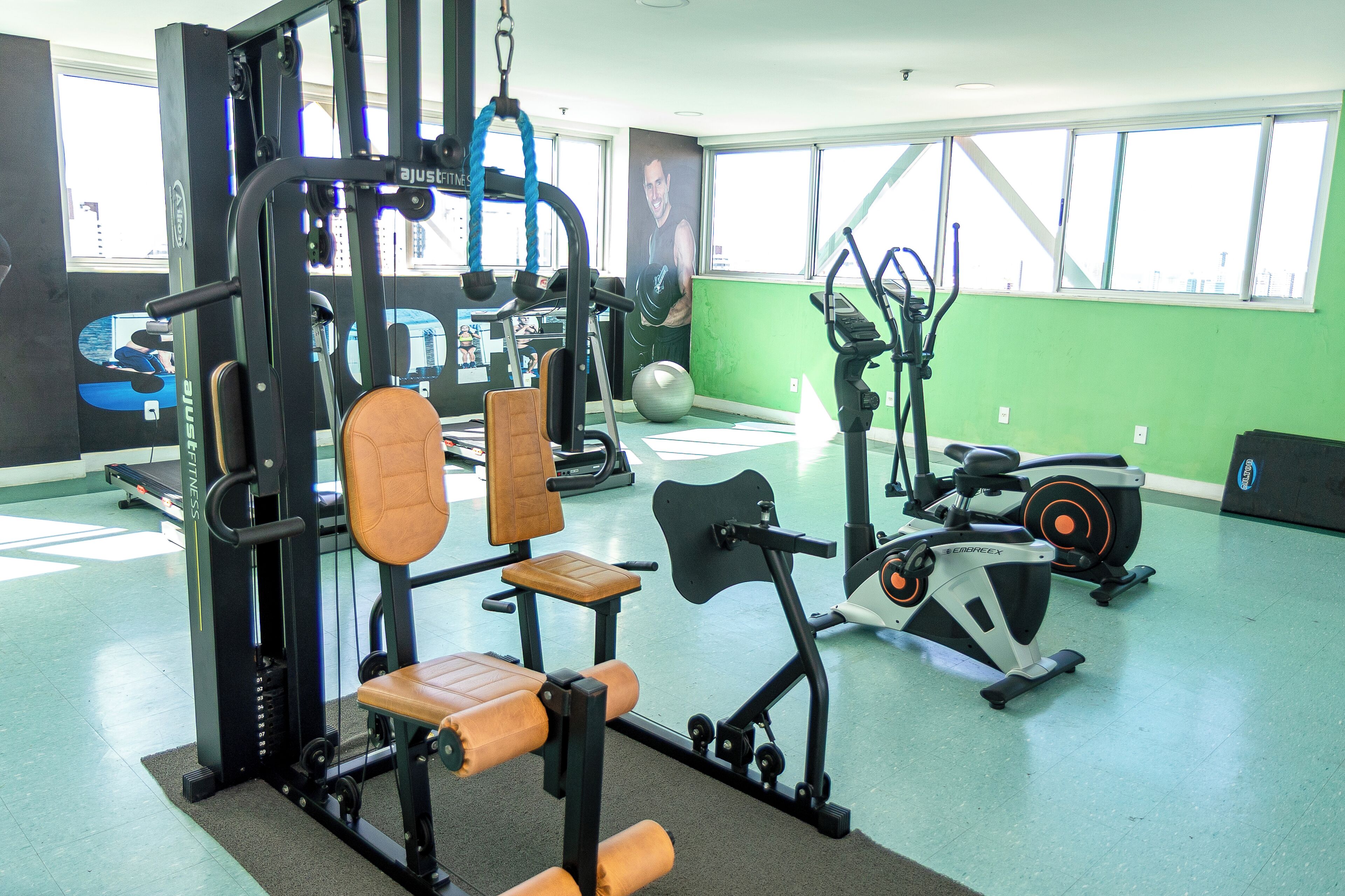 Uma academia com equipamentos de exercícios, uma janela grande e uma parede verde.