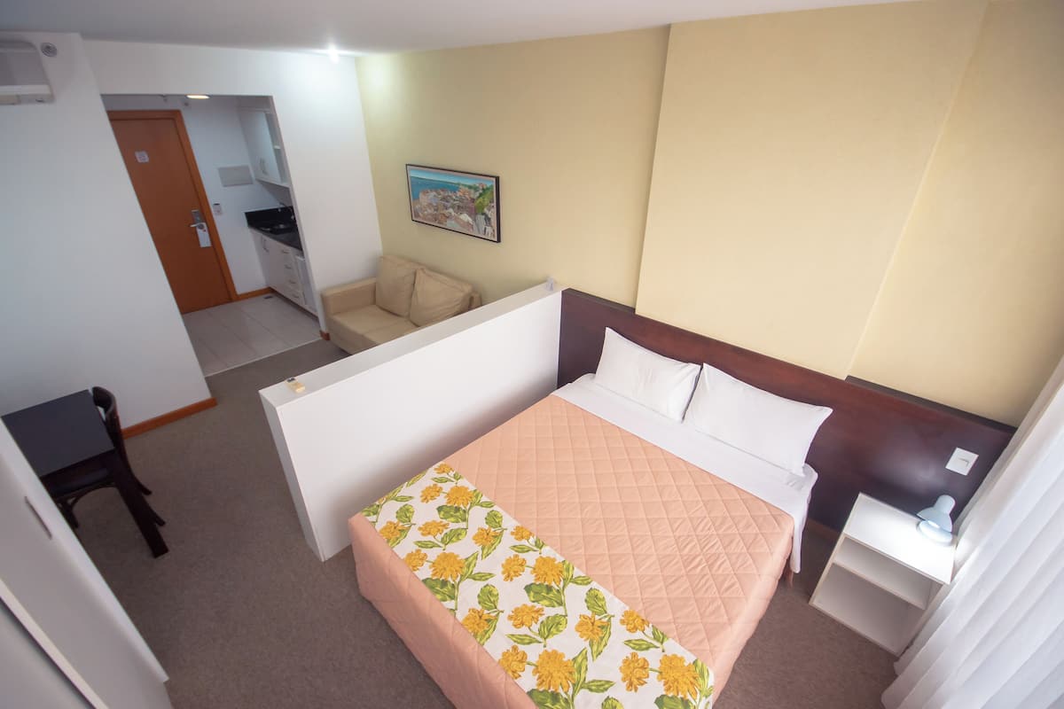 Een hotelkamer met een bed, een bureau, een stoel, een kleine kitchenette en een schilderij aan de muur.