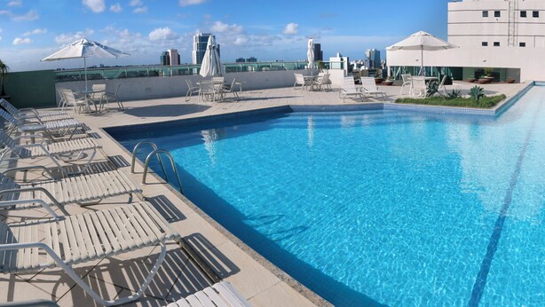 A rooftop swimming pool with lounge chairs and umbrellas, surrounded by modern buildings.