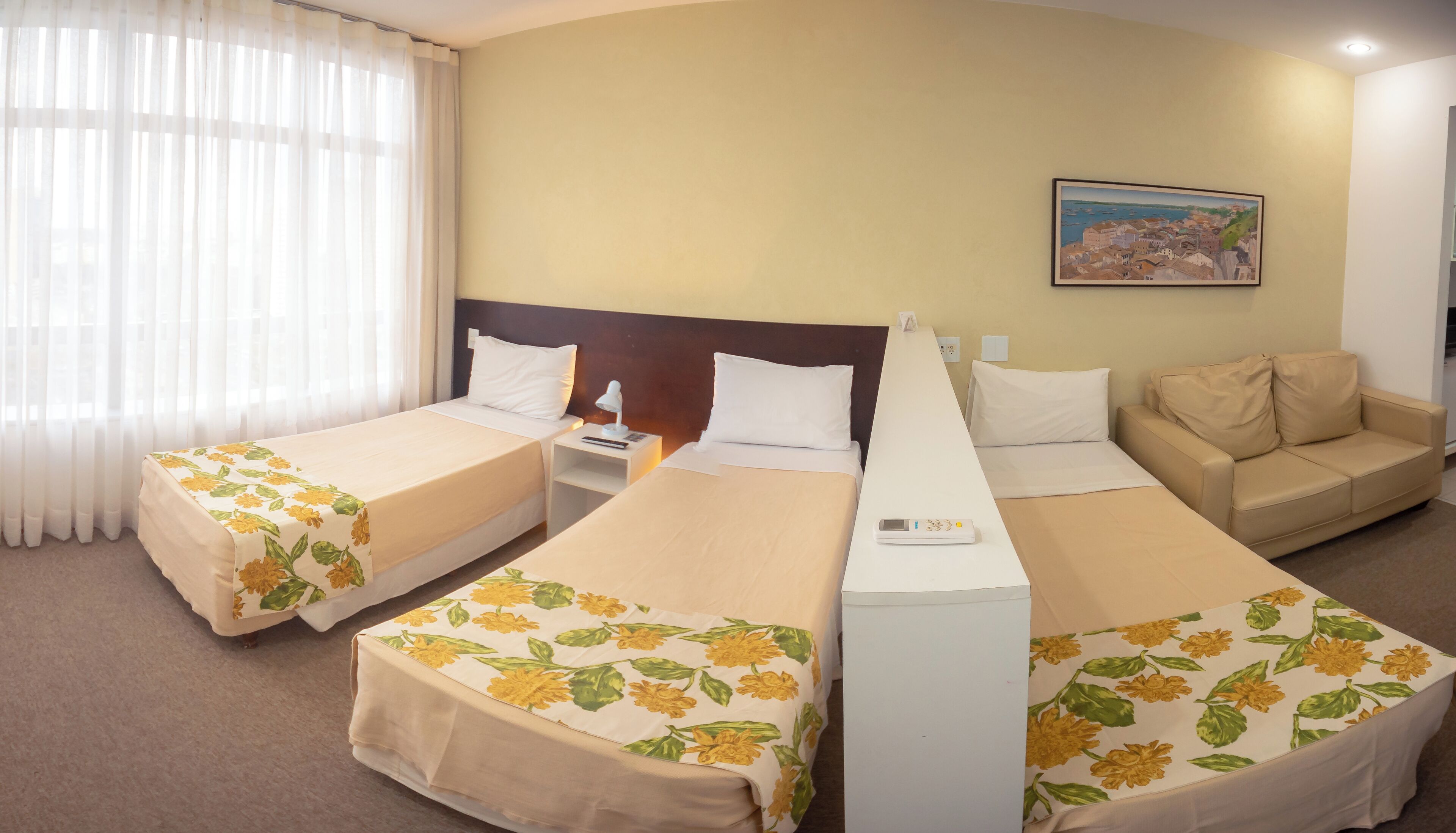 A hotel room with two single beds, a sofa, a nightstand, and a painting on the wall.