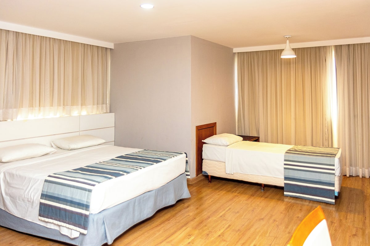 A hotel room with two beds, a wooden floor, and a large window with curtains.