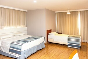 A hotel room with two beds, a wooden floor, and a large window with curtains.