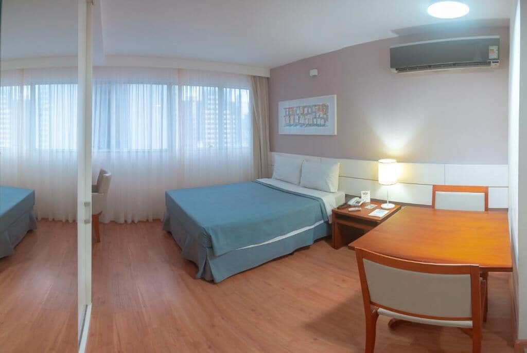 A hotel room with two single beds, a wooden dining table, a nightstand, and a wall-mounted air conditioner.