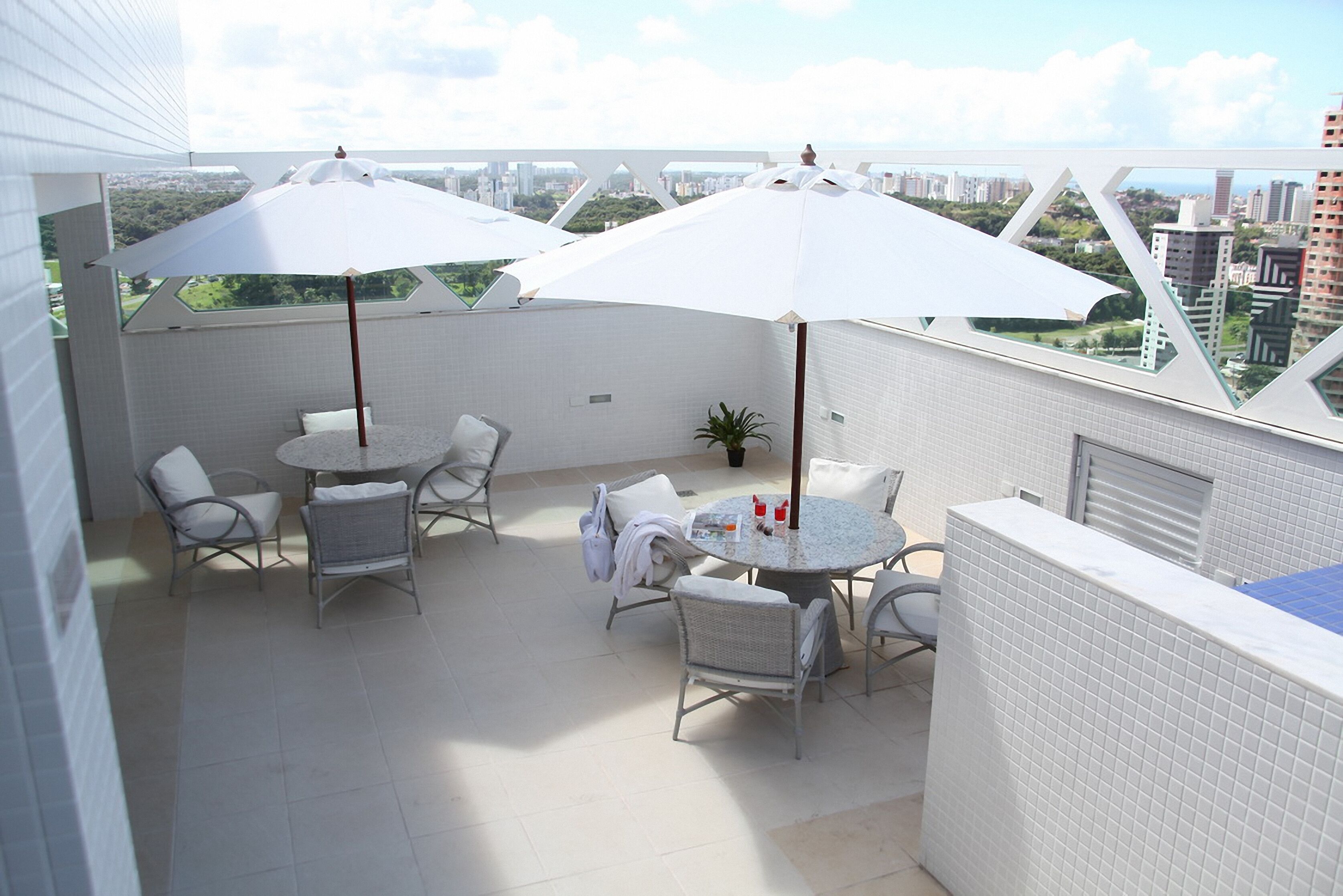 A rooftop terrace with a round table and chairs, two white umbrellas, and a view of the cityscape.