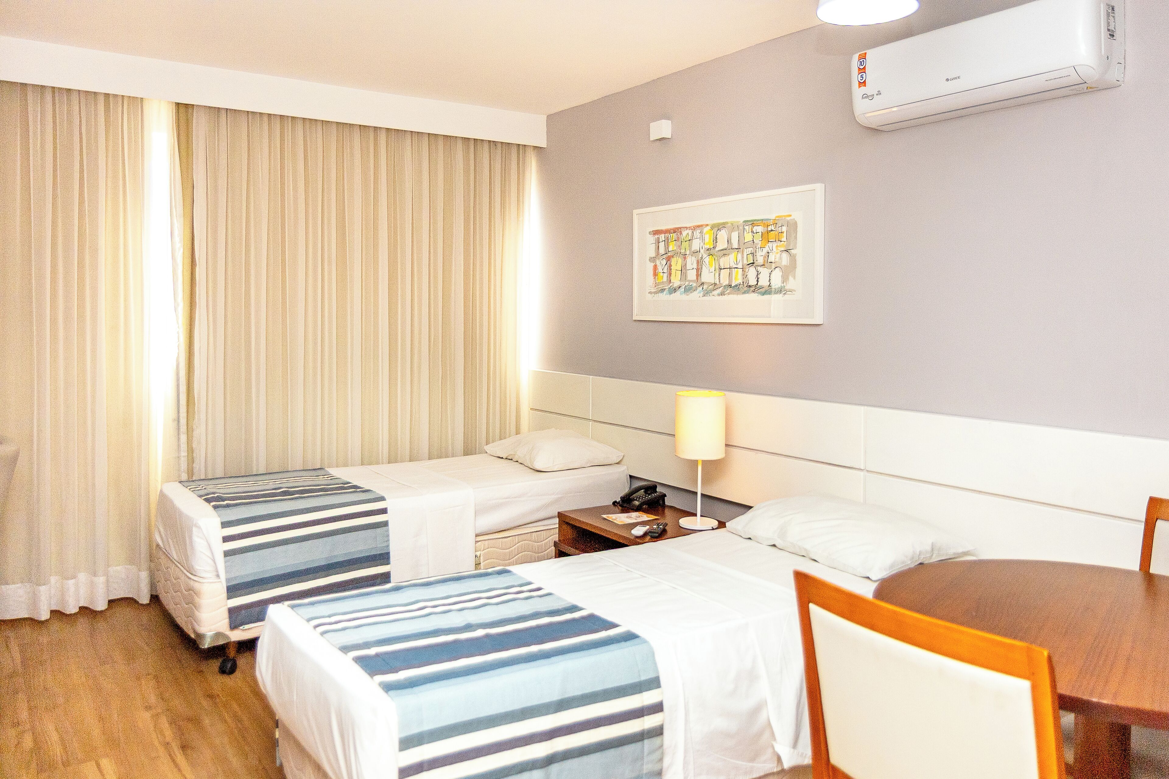 Een hotelkamer met twee bedden, een nachtkastje met een lamp, een houten stoel en een schilderij aan de muur.