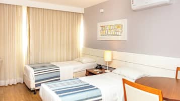 Een hotelkamer met twee bedden, een nachtkastje met een lamp, een houten stoel en een schilderij aan de muur.