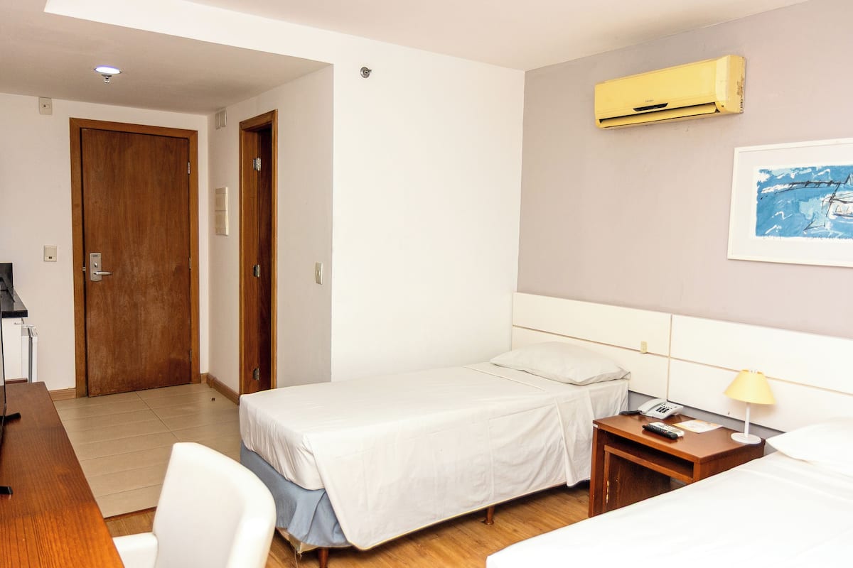A hotel room with a bed, bedside table, lamp, and an air conditioner.