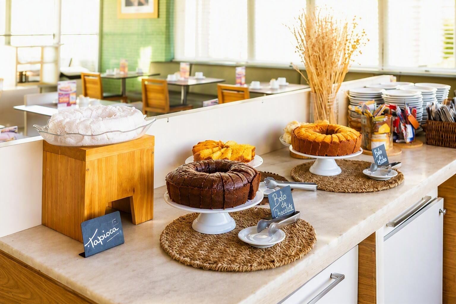Zona de bufé con diversos postres expuestos en mesas, una barra de madera y un cartel que indica opción de pastel de chocolate.