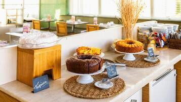 Zona de bufé con diversos postres expuestos en mesas, una barra de madera y un cartel que indica opción de pastel de chocolate.