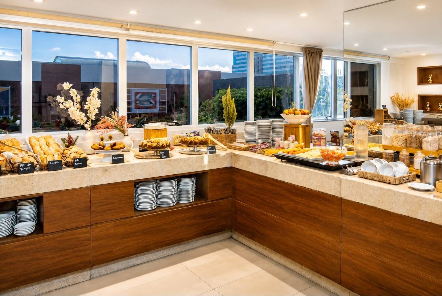 Eine moderne Küche mit Frühstücksbuffet, Holzschränken und großen Fenstern mit Blick auf die Stadt.