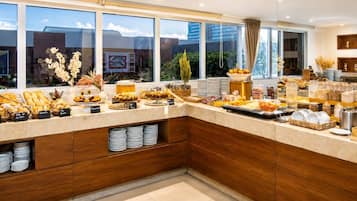 Una cocina moderna con bufé de desayuno, armarios de madera y grandes ventanales con vistas a la ciudad.