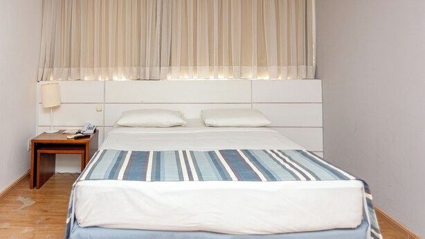 A bedroom with a bed, two pillows, a bedside table with a lamp, and a nightstand with a phone.