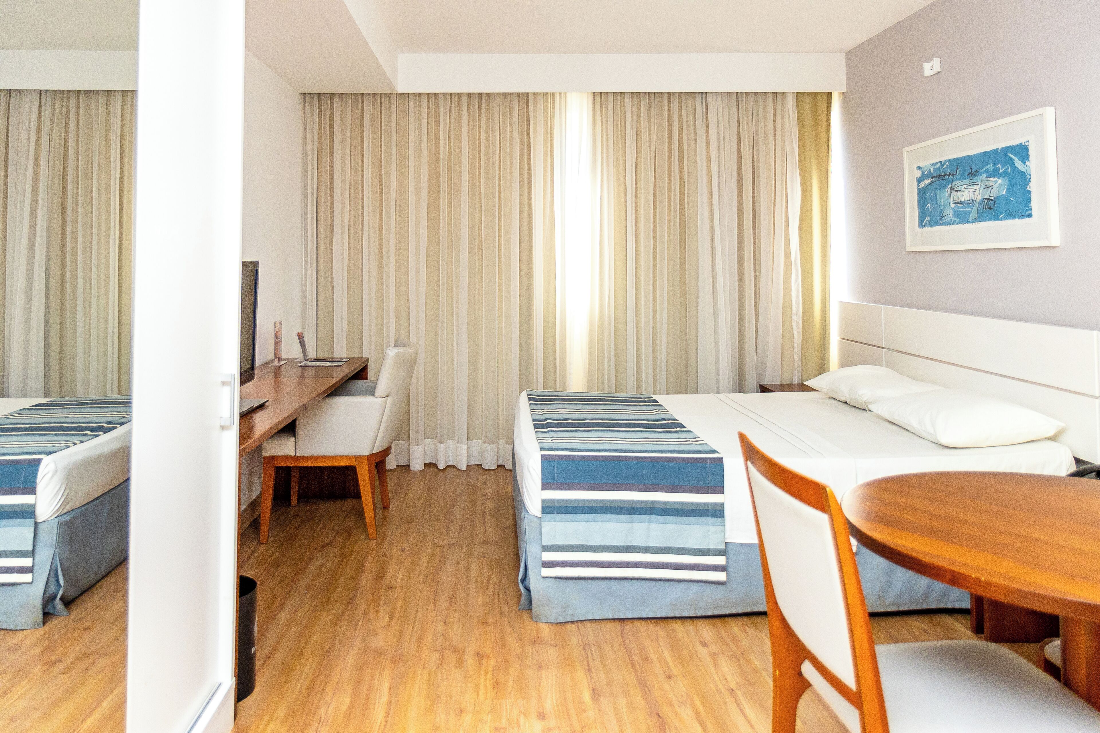 A hotel room with two beds, a desk, a chair, and a dining table.