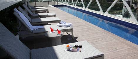A rooftop pool area with lounge chairs, a small table with a magazine and sunglasses, and a view of the cityscape.