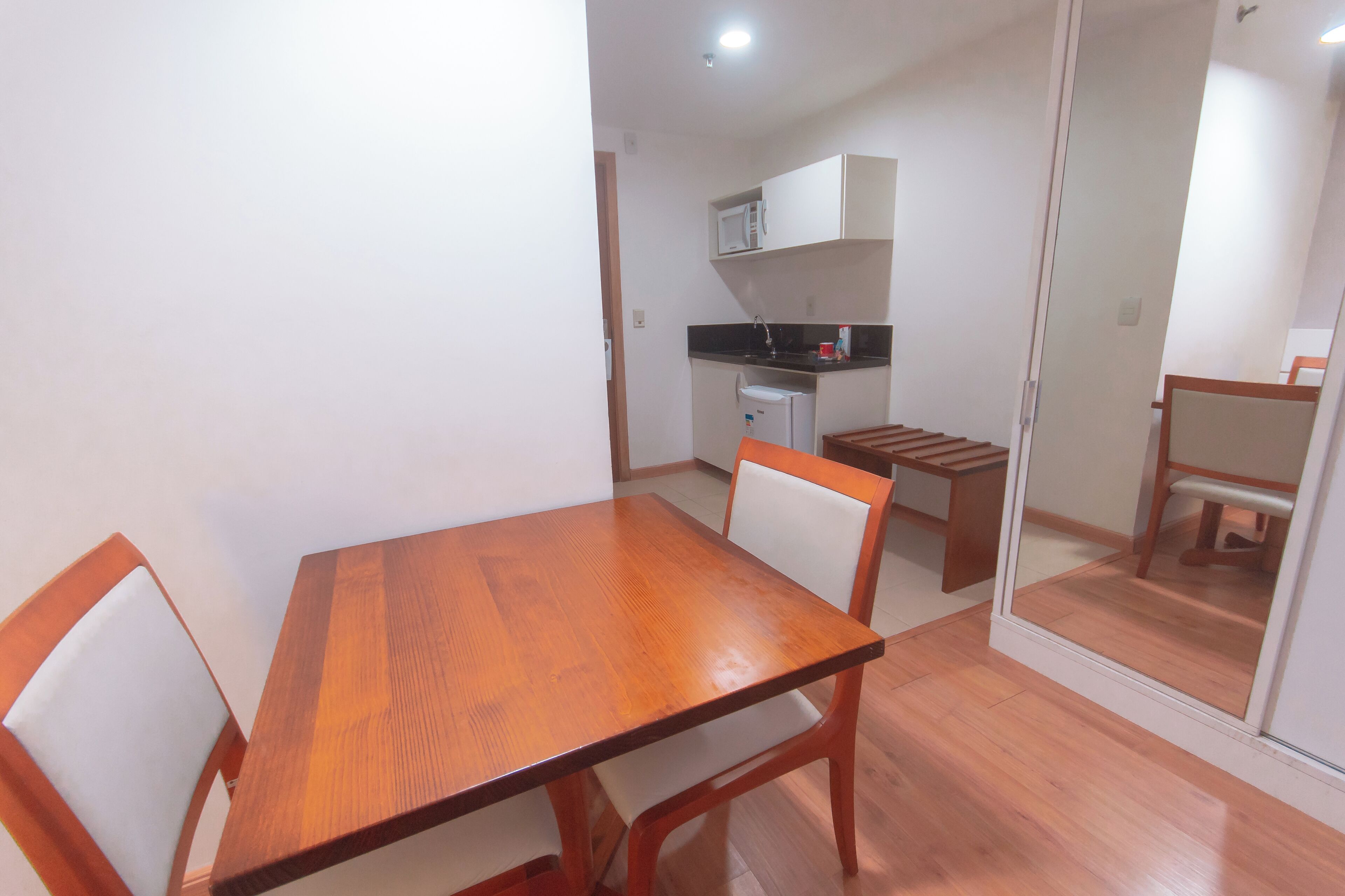 Comedor con mesa y sillas de madera, cocina al fondo y puerta corredera que da a otra habitación.