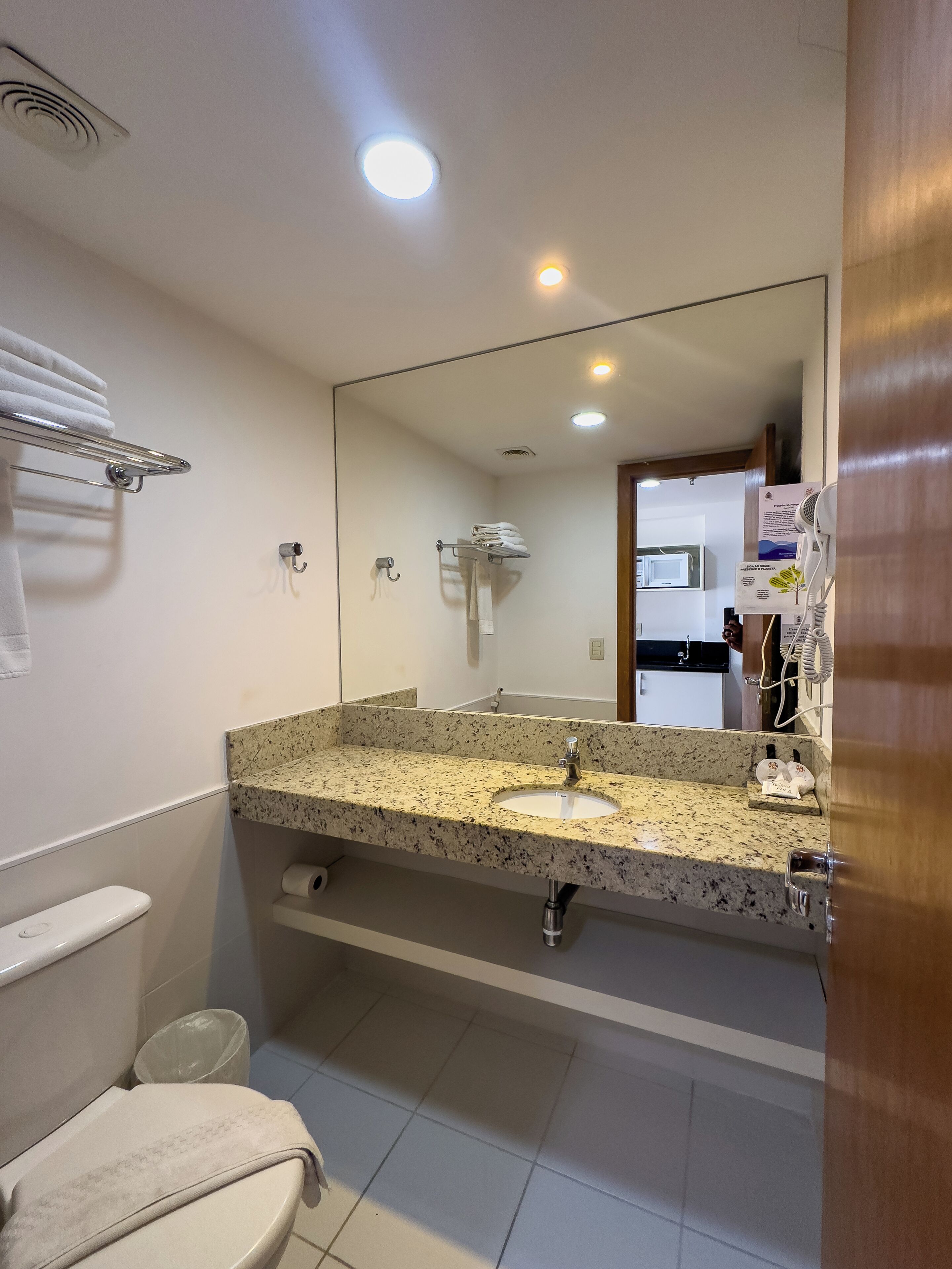 A bathroom with a granite countertop sink, a mirror, a towel rack, and a toilet.