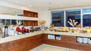 Un bar à petit-déjeuner moderne, doté d’un comptoir en bois, de divers aliments pour le petit-déjeuner et de plantes décoratives.