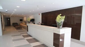 Un espace d’accueil moderne avec un sol à carreaux, un comptoir d’accueil, un coin salon et une grande fenêtre.