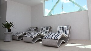 Une véranda avec trois fauteuils de relaxation en osier, une plante en pot et une grande fenêtre donnant sur le ciel.