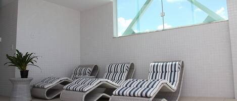 Un solarium con tres sillones de mimbre, una planta en maceta y un amplio ventanal con vistas al cielo.