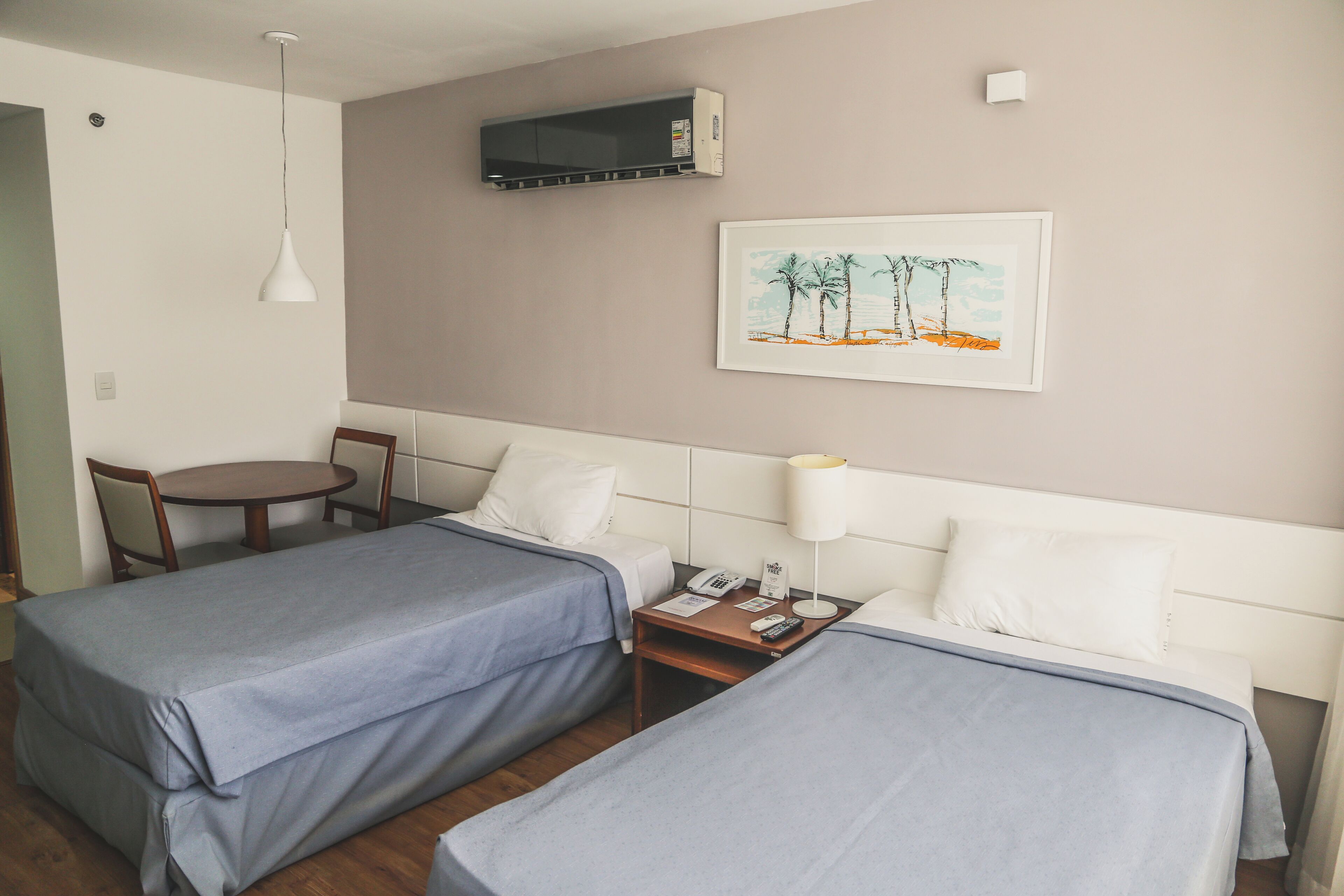 Habitación de hotel con dos camas, un escritorio, una silla, una lámpara y un cuadro en la pared.