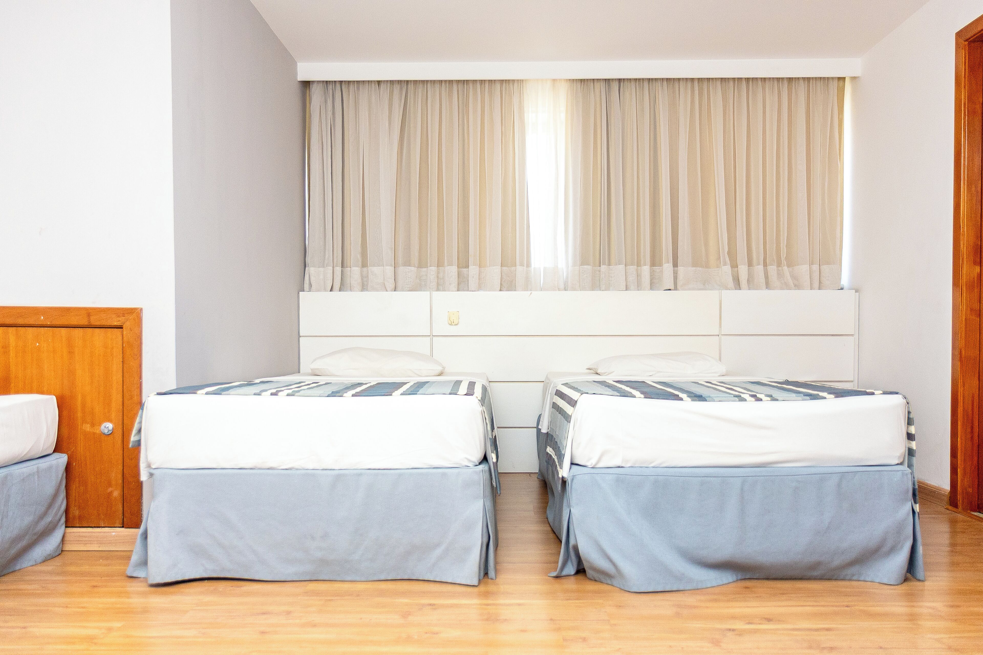 A room with two beds, a wooden door, and a window with curtains.