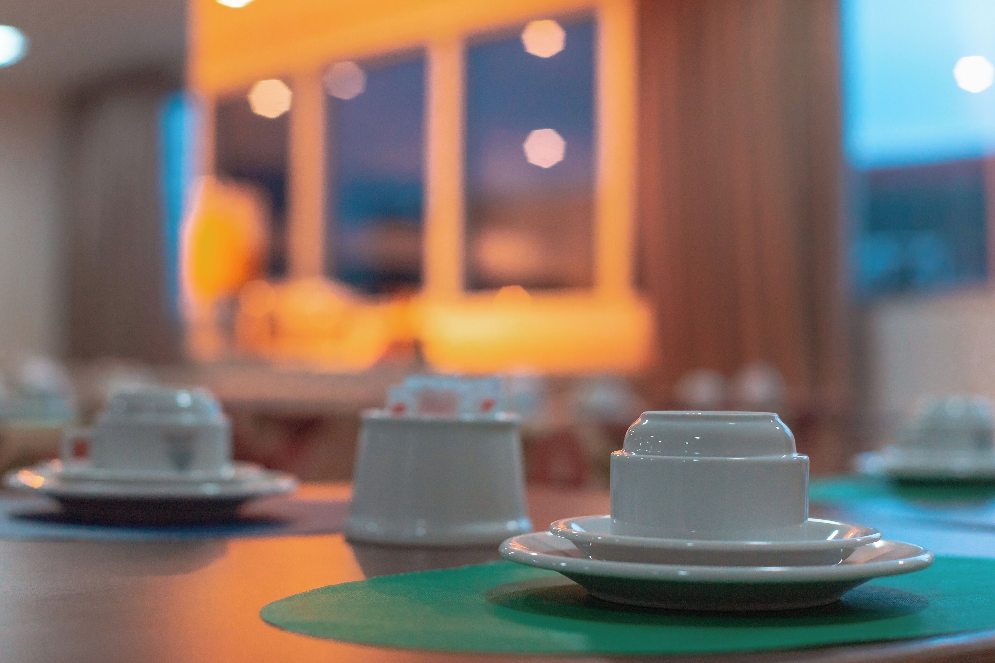 A table with white teapots and cups on green placemats.
