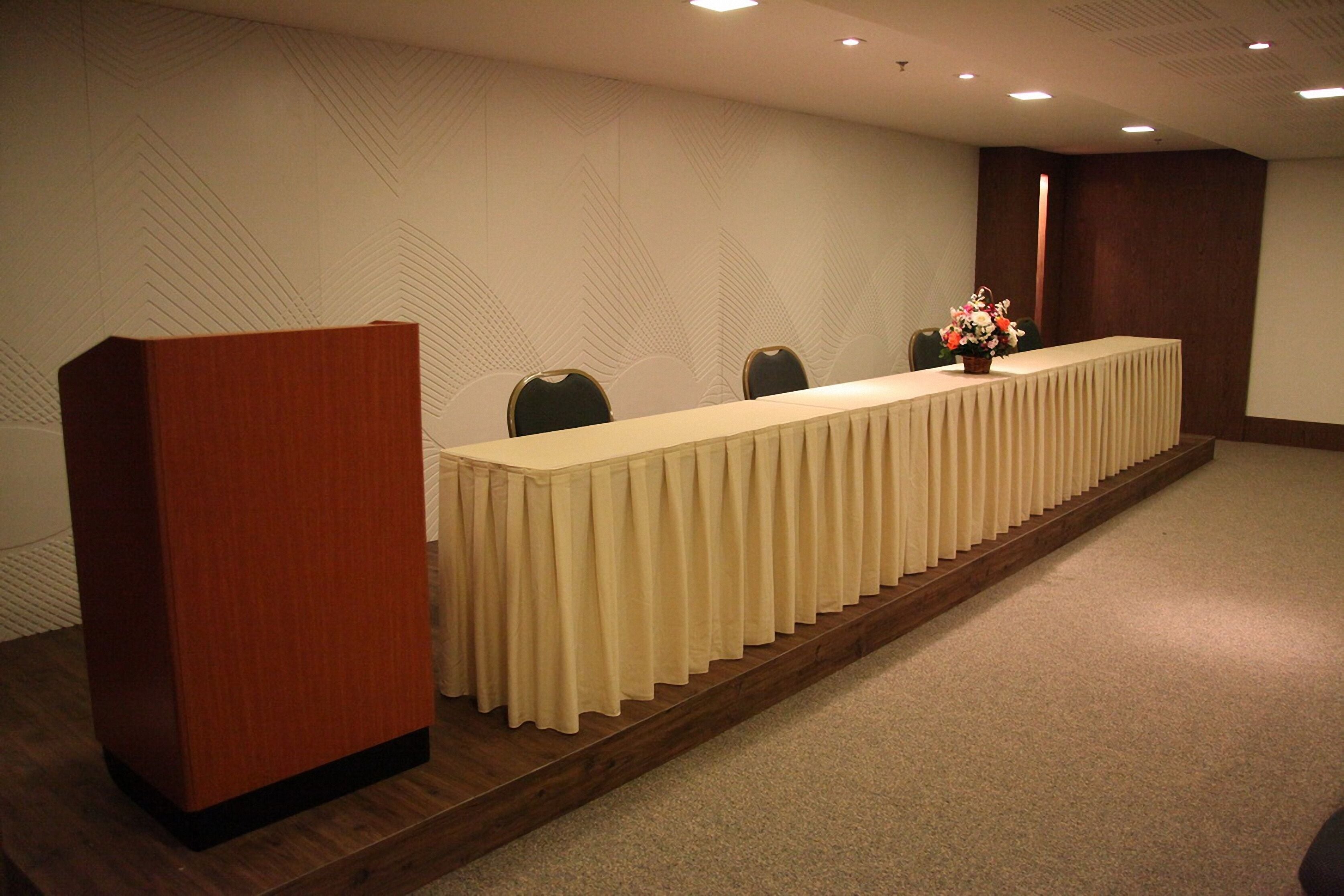 A conference room with a long table, chairs, a podium, and a floral arrangement.