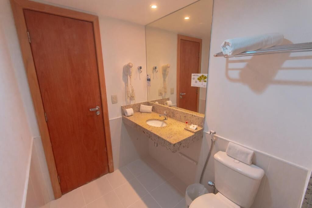 Une salle de bain avec une porte en bois, un lavabo surmonté d’un miroir et un porte-serviettes.