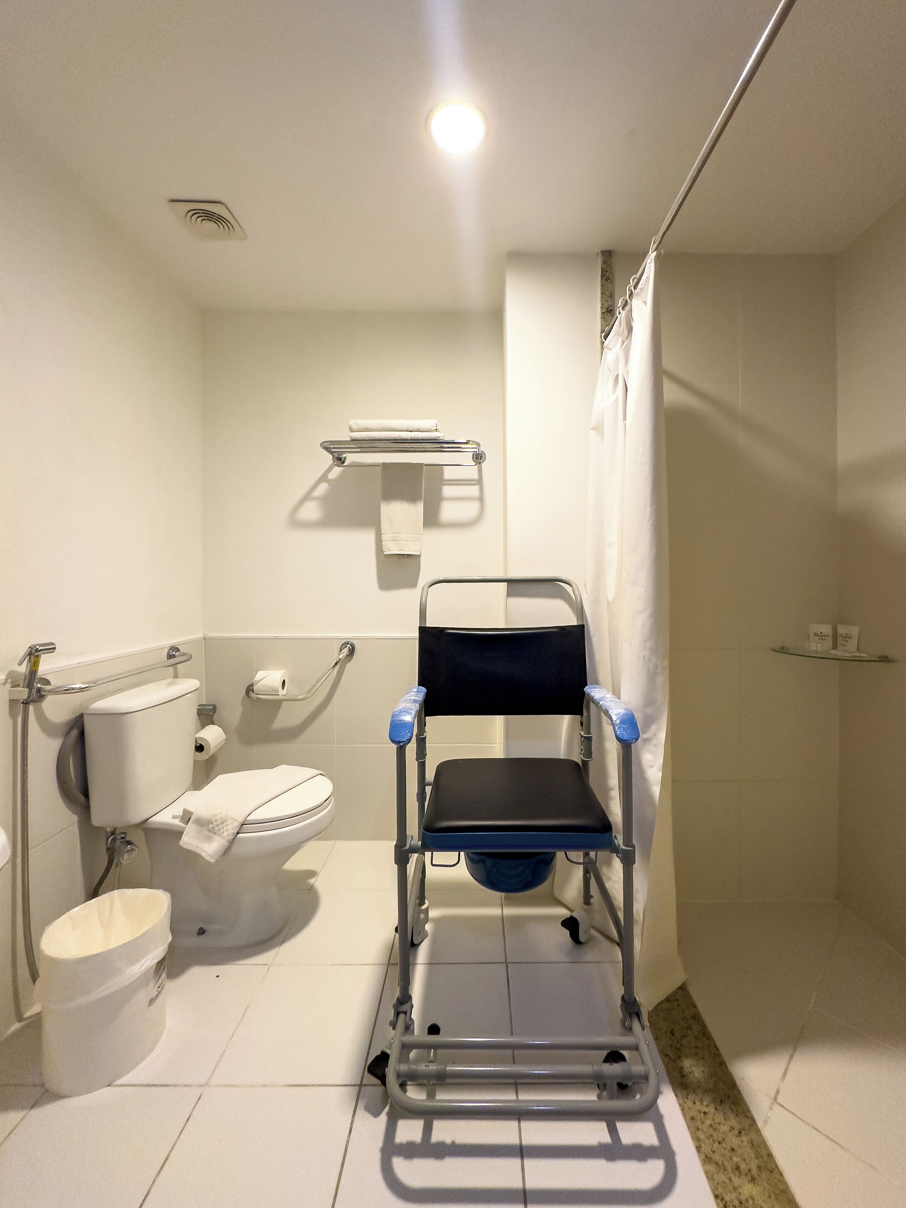 Une salle de bain accessible aux personnes en fauteuil roulant, équipée de toilettes, d’une barre d’appui et d’un espace douche.