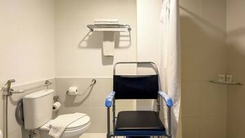 Un baño accesible en silla de ruedas, con inodoro, barandilla y zona de ducha.