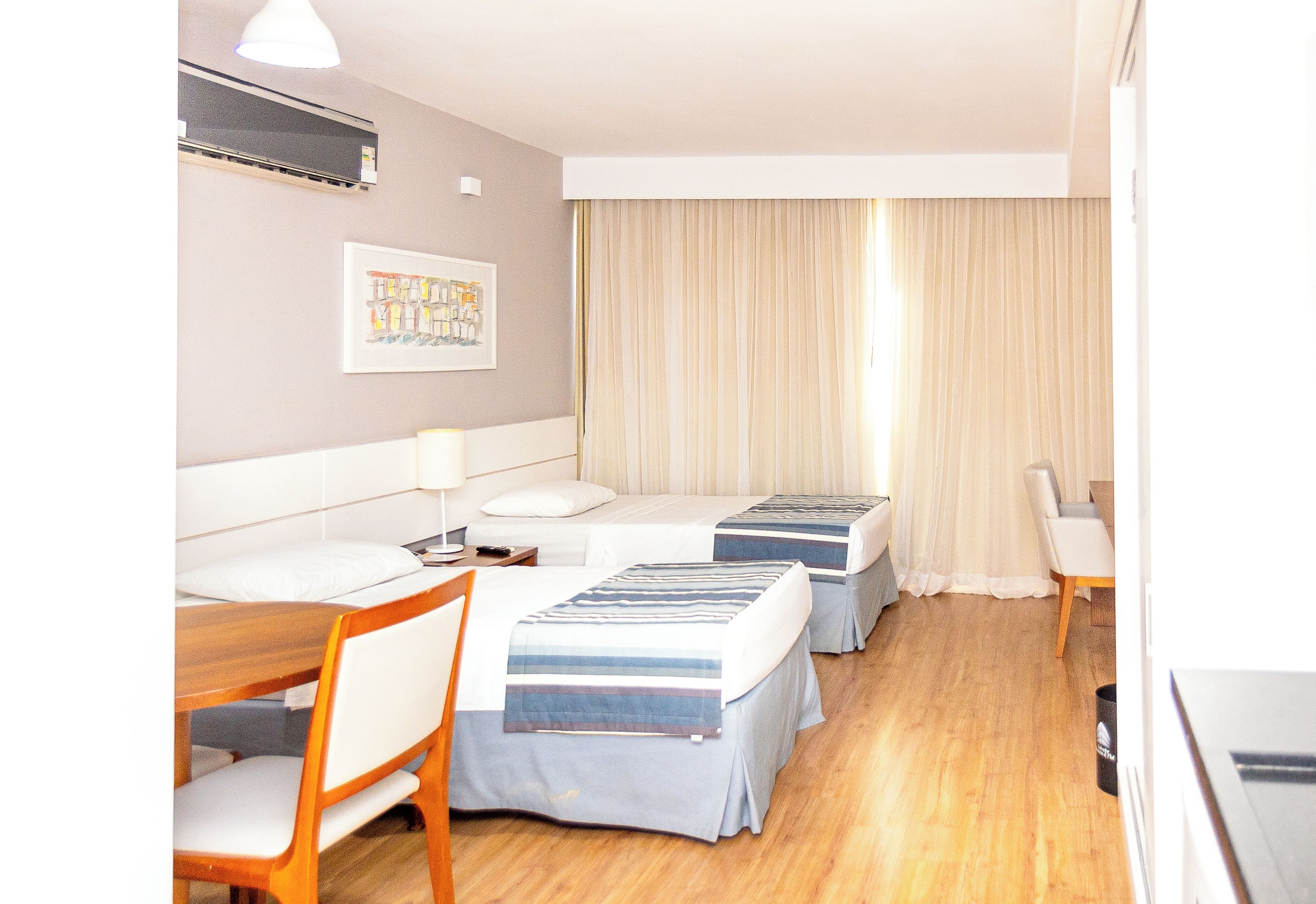 Habitación de hotel con dos camas, un escritorio, una silla, una lámpara y un cuadro en la pared.