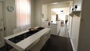 A modern kitchen with white cabinetry, a dining area with a white table and chairs, and a visible clock on the wall. - Alexandra Place (Bendigo)