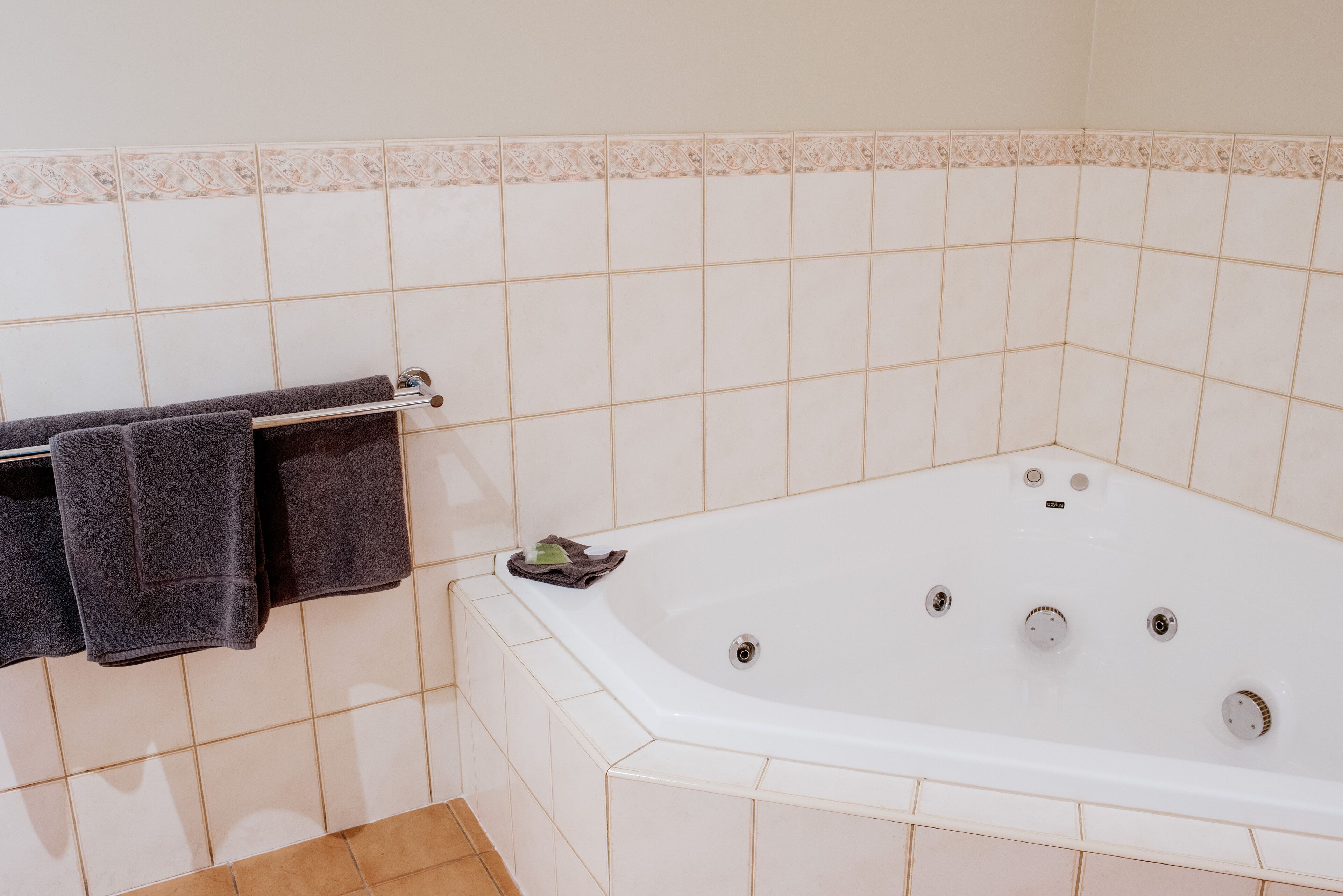 Une salle de bain avec une baignoire blanche, un porte-serviettes avec des serviettes et un sol carrelé.