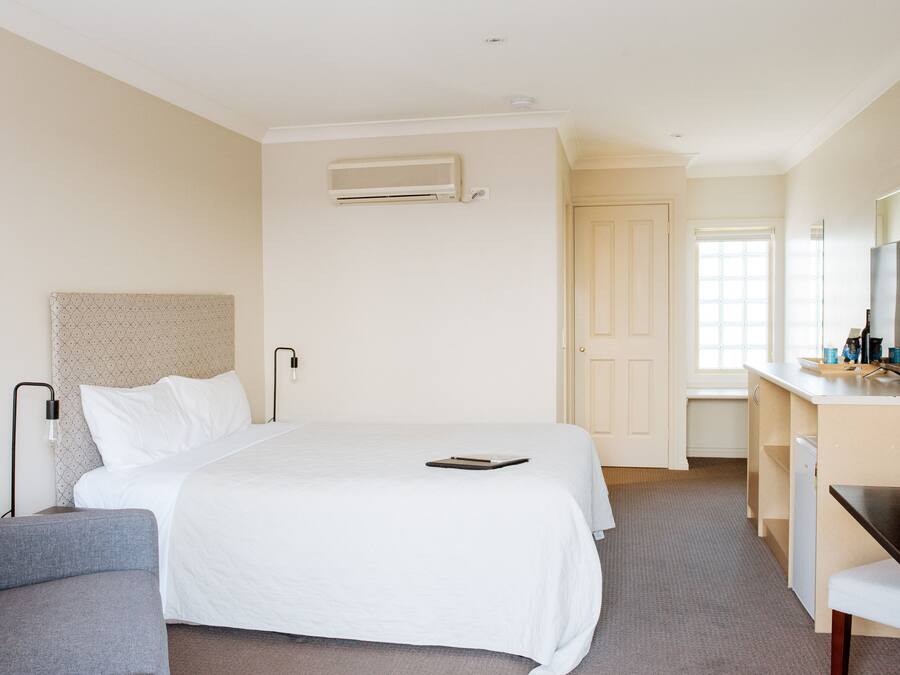 A hotel room with a bed, a desk, a chair, a small table, and a TV.