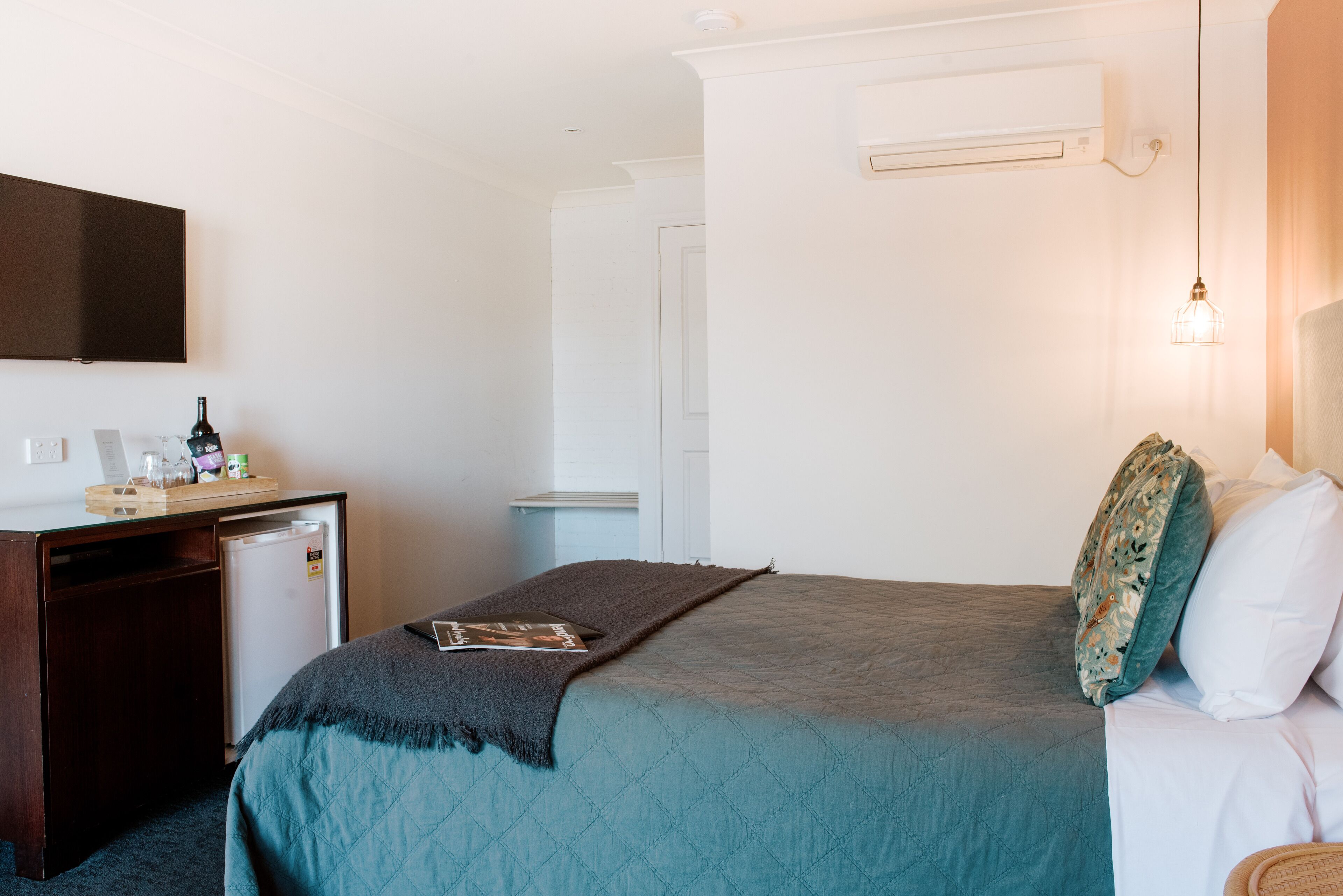 Habitación de hotel con cama, escritorio con refrigerador, televisor de pantalla plana y aire acondicionado de pared.