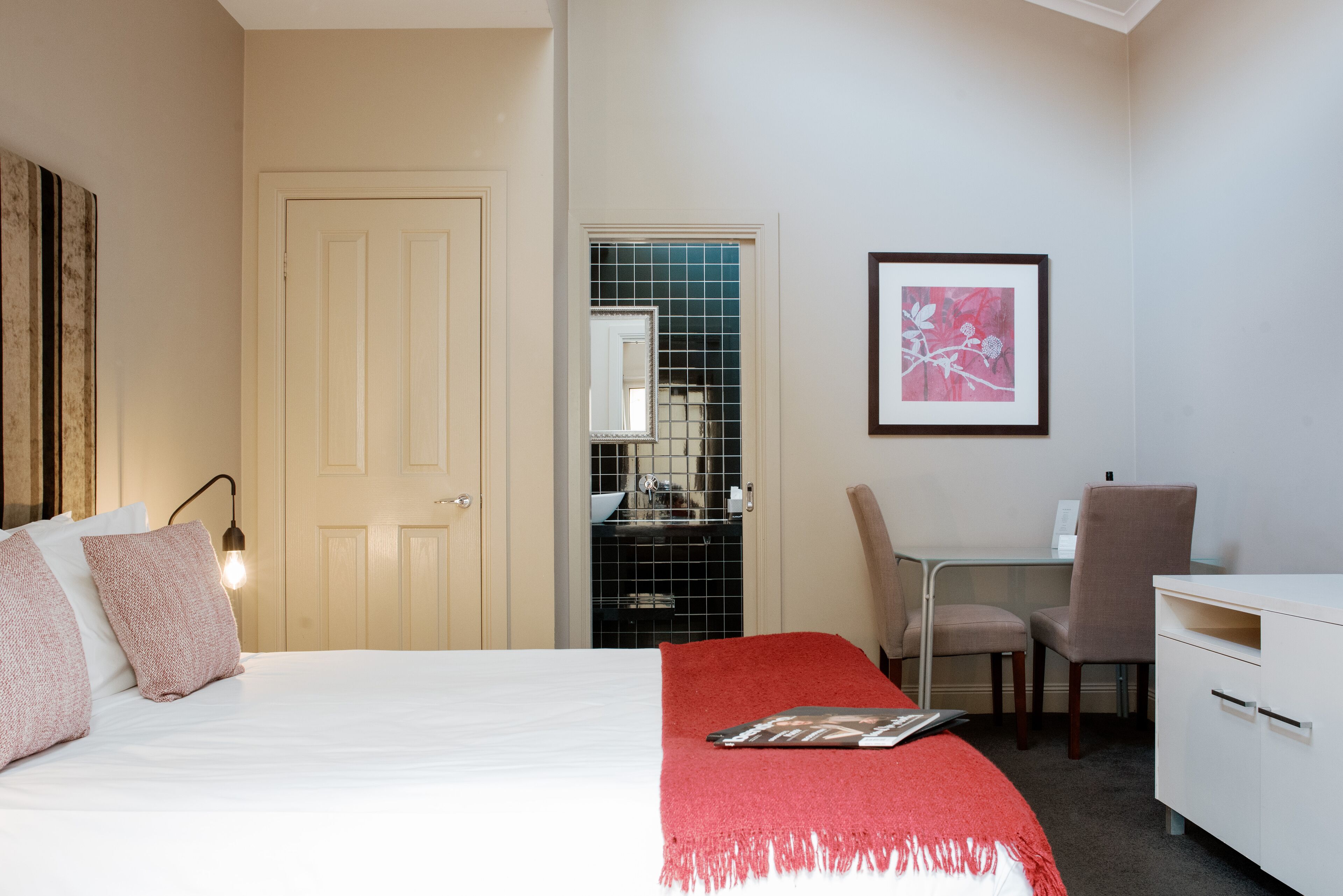 Habitación de hotel con cama, escritorio, silla, armario y un cuadro en la pared.
