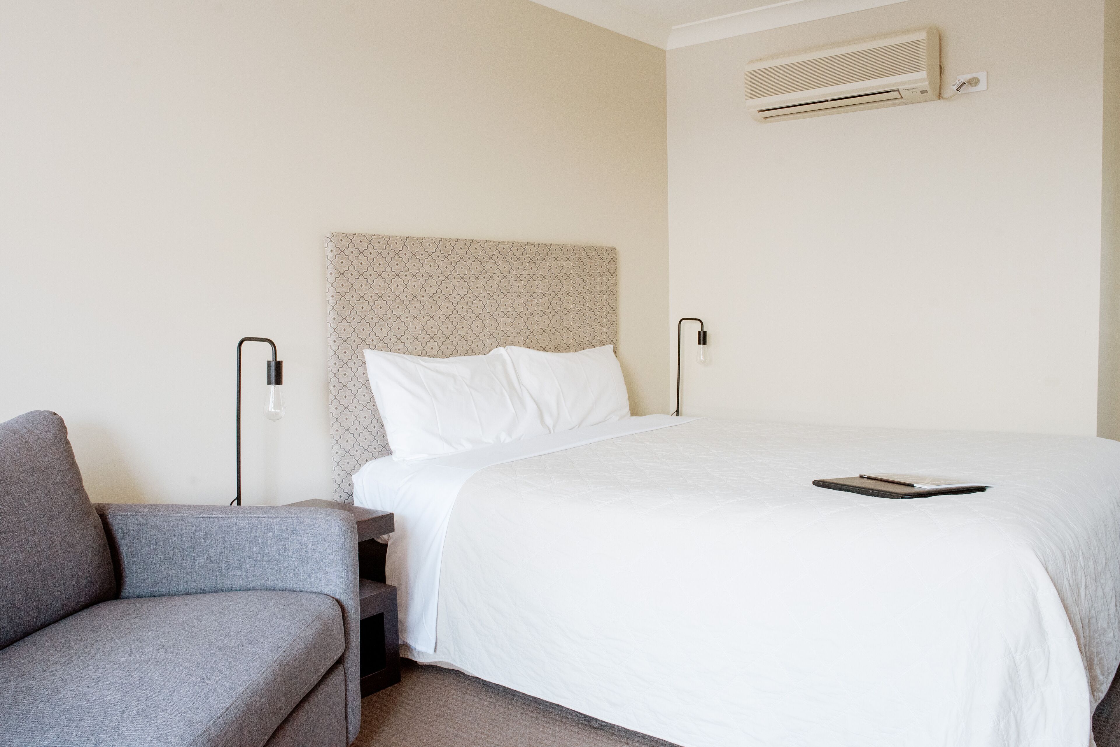 Et hotelværelse med en seng, en grå sofa, et natbord og en vægmonteret aircondition.
