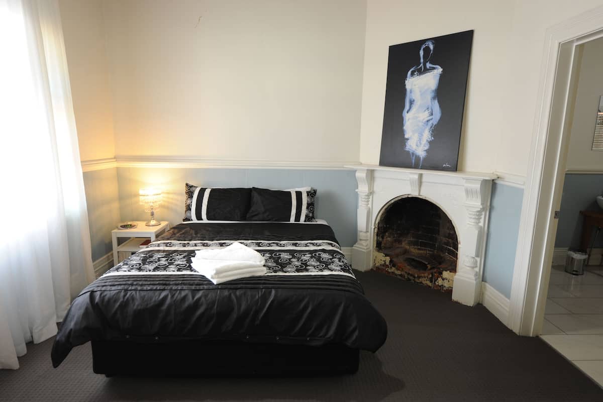 A bedroom with a large bed, a fireplace, and a painting on the wall.