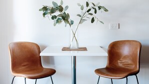 A white table with two brown leather chairs, a vase with green leaves, and a power outlet on the wall. - Alexandra Place (Bendigo)