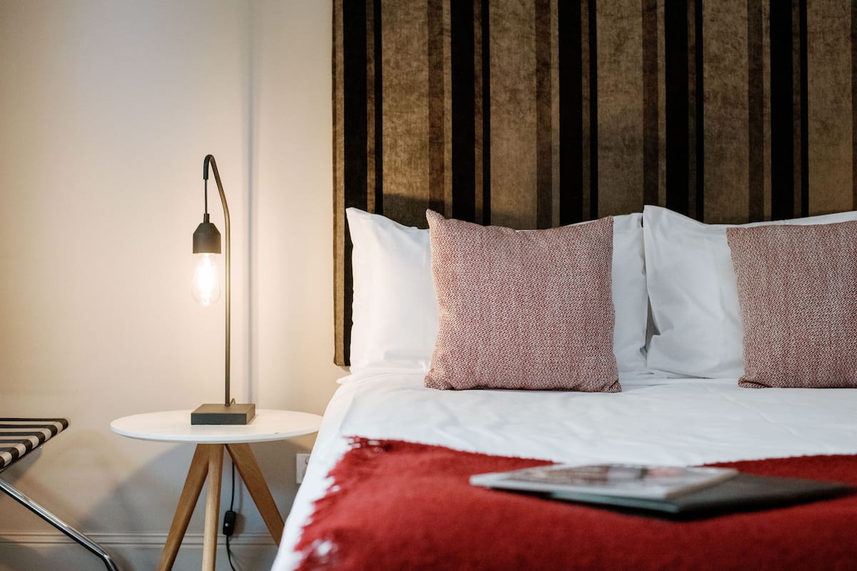 A neatly made bed with white and red pillows, a red throw blanket, and a bedside table with a lamp.