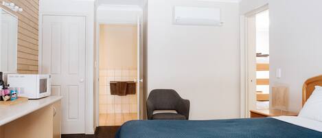 Una habitación de hotel con una cama, un escritorio con microondas, una silla y una mesita de noche con lámpara.