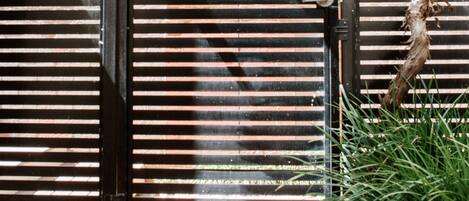 A closed metal gate with horizontal slats, a brick wall in the background, and a vine growing over the gate.