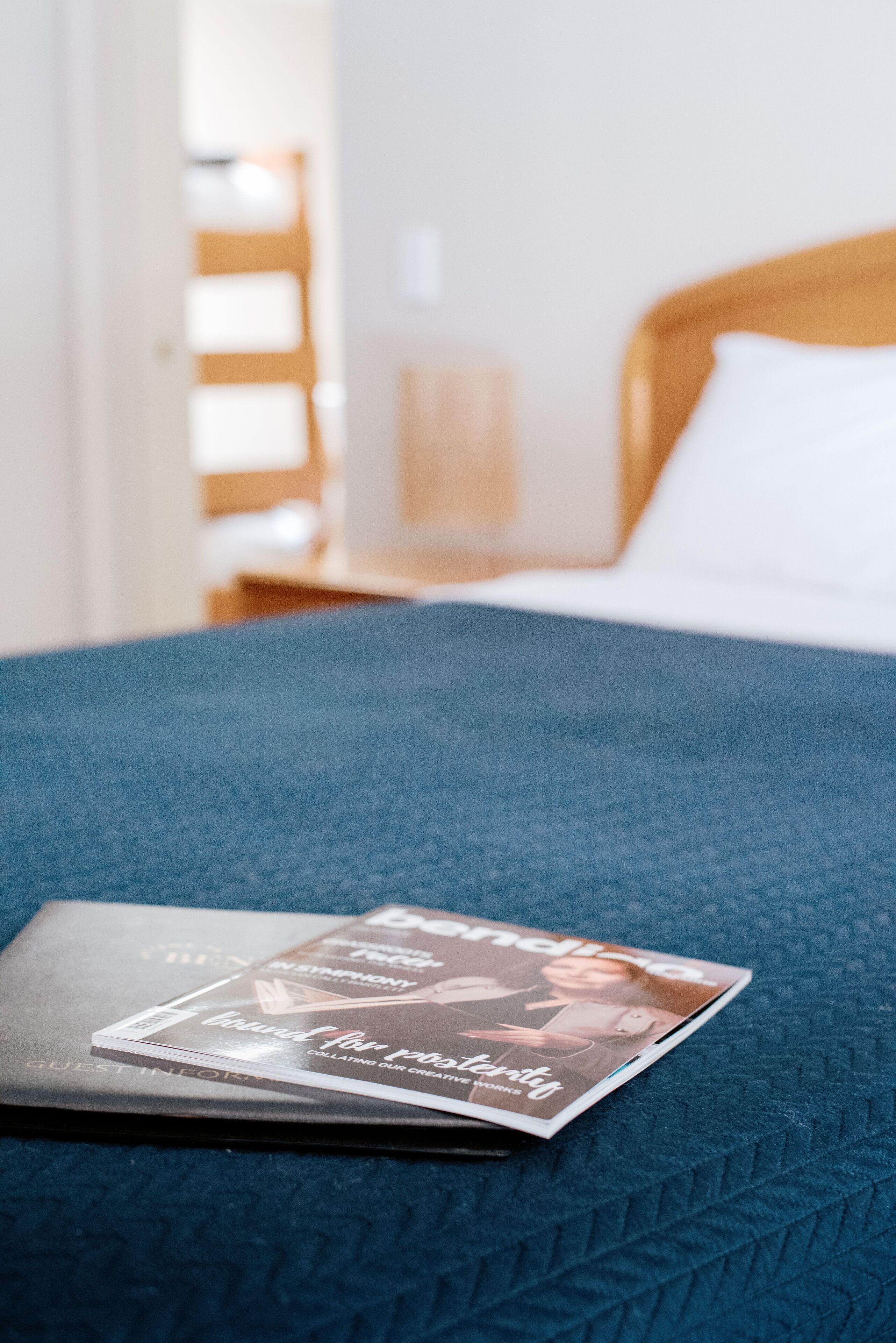Una cama con colcha azul, una revista encima y un cabecero de madera.