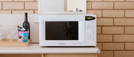 Un horno microondas blanco sobre una encimera de madera, con un fondo de pared de ladrillo.