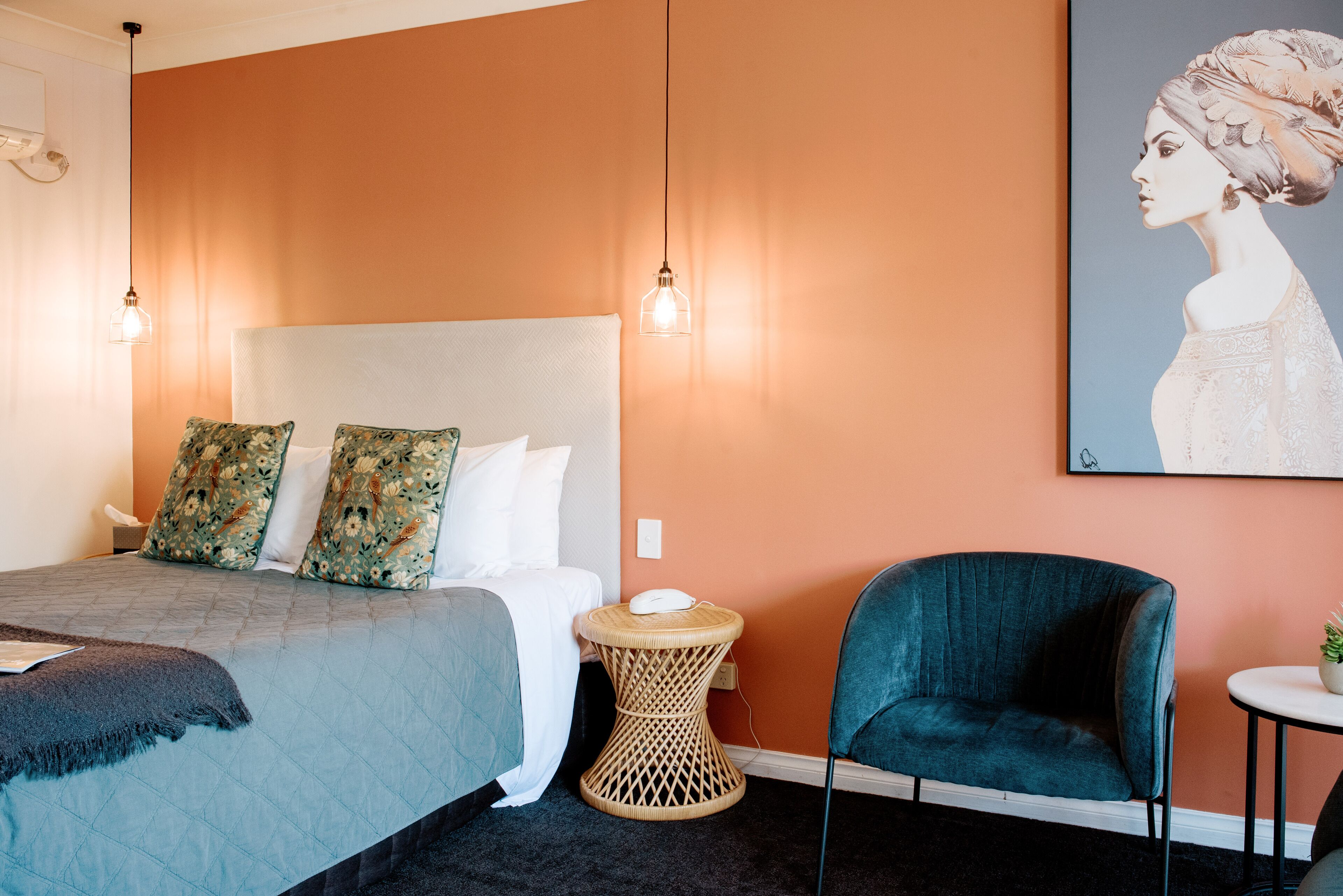 Quarto de hotel com cama, mesa lateral redonda, uma cadeira e um quadro na parede.