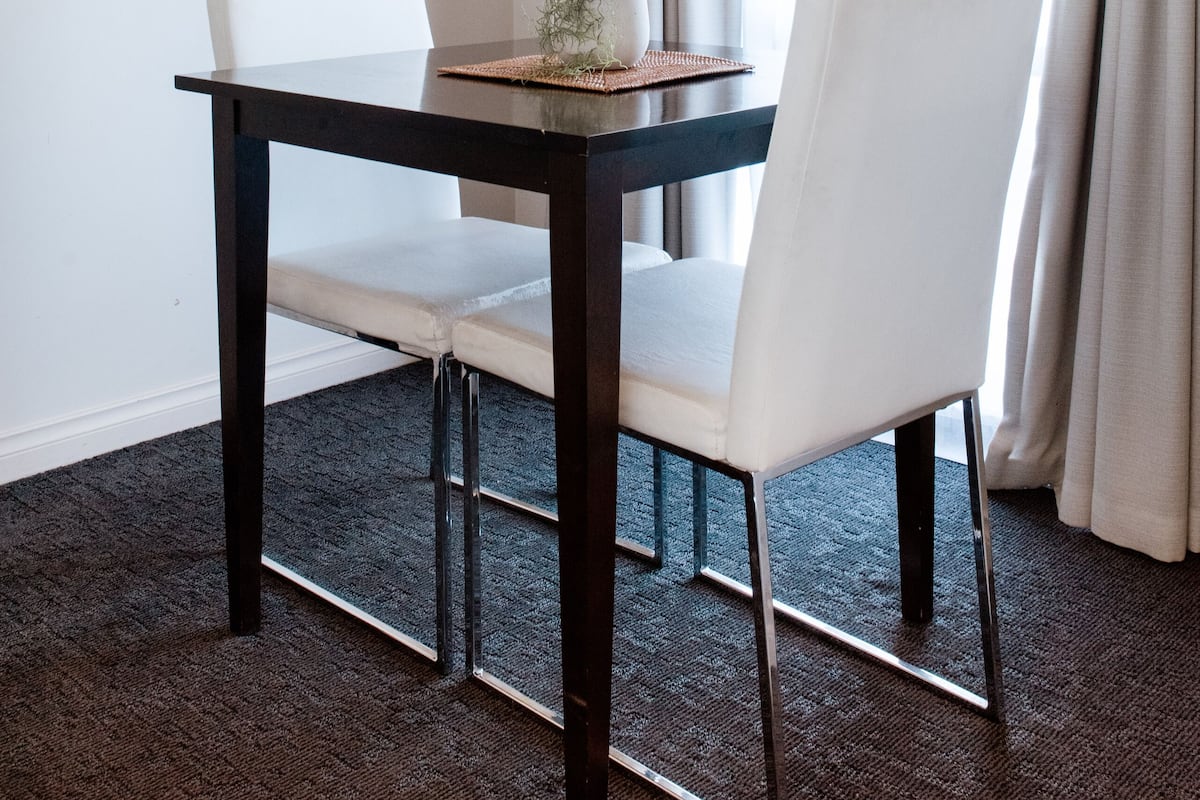 A dining area with a dark wooden table, white chairs, and a small plant on the table.
