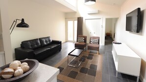A modern living room with a black leather sofa, a coffee table, and a TV mounted on the wall. - Alexandra Place (Bendigo)