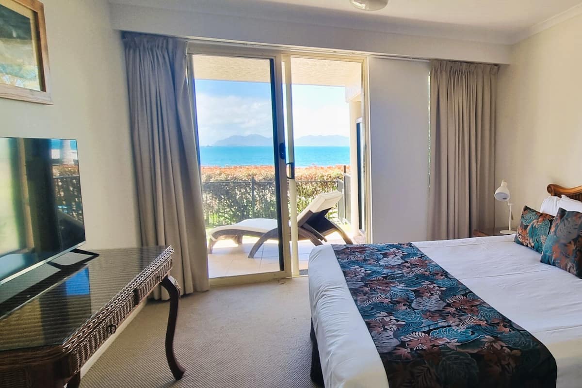 A hotel room with a bed, a TV, a balcony with a view of the sea, and a chair.